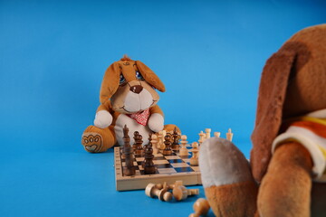 Close up of toy doggies with chess pieces on chessboard. Soft plush toys playing chess on blue background.
