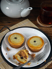 Putu belanda is Indonesian cookies which has vla filling, crashed peanut, and topping with raisin. Served in white plate on tray along with teapot and glass of tea. Concept on snacking or tea time. 