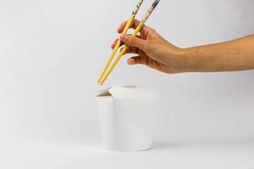 hand with chopsticks and cardboard food box on white background