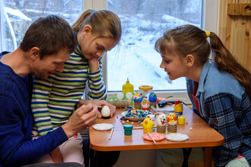 Children carefully watch their dad paint eggs