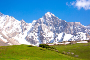 A beautiful natural mountain landscape in spring with green grass, in a valley with a blue sky on...