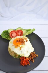 Nasi goreng or Indonesian fried rice with egg garnished with  lettuce, fresh cucumber slices , slice tomato, fried onion, sambal and sunny side up 