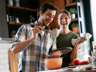 Husband and wife making pancakes at home. Loving couple having fun while preparing food..