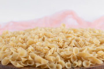 Bunch of various pasta on wooden plate with pink cloth