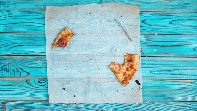 Stop motion animation of eating pizza on baking paper on blue wooden background.