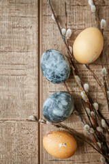 Beige and gray Easter eggs and pussy willow sprigs lie on a brown wooden surface. Copy Space