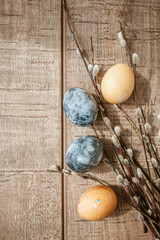 Beige and gray Easter eggs and pussy willow sprigs lie on a brown wooden surface. Copy Space