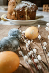 Fototapeta na wymiar Beige and gray Easter eggs and pussy willow sprigs lie on a brown wooden surface near the Easter cake