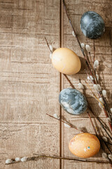 Beige and gray Easter eggs and pussy willow sprigs lie on a brown wooden surface. Copy Space