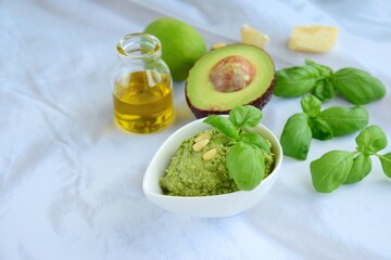 Basil avocado pesto sauce with main ingredients: fresh basil leaves, avocado, parmesan cheese, pine nuts, garlic and lime