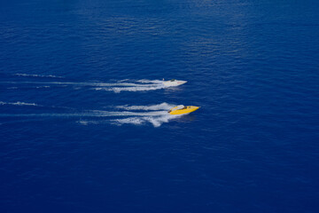 Fototapeta na wymiar Two speed boats of white and yellow color fast motion on blue water top view. Speed boats movement at high speed aerial view. Aerial view luxury motor boat.