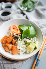 Closeup view of a delicious poke bowl full of chopped salmon and avocado pieces mixed with rice and spinach leaves.