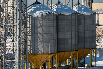 silver silos on agro manufacturing plant for processing drying cleaning and storage of agricultural products, flour, cereals and grain. The granary silo of the elevator is covered with snow in winter