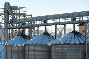 silver silos on agro manufacturing plant for processing drying cleaning and storage of agricultural products, flour, cereals and grain. The granary silo of the elevator is covered with snow in winter © Pokoman