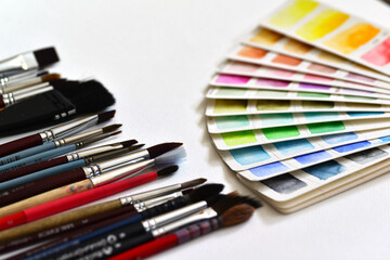 Obraz premium Watercolor color palette on white paper, fanned out, next to a set of brushes. On a white paper background.