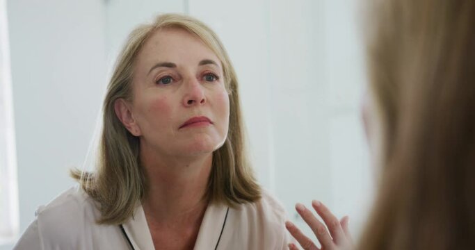 Caucasian senior woman looking in bathroom mirror inspecting her face