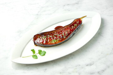 Baked eggplant in josper with miso sauce, cilantro, nuts and sesame seeds. Miso eggplant in a white plate on a marble background. View from above