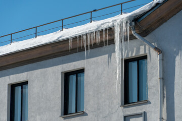 The roofs of the buildings are covered with snow and ice after a big snowfall. Huge icicles hang from the facades of buildings. The fall of icicles carries a danger to people's lives.