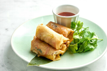 Asian street food - Deep-fried spring roll in rice paper served in a beige plate with spicy chili sauce on a marble background. Restaurant food.