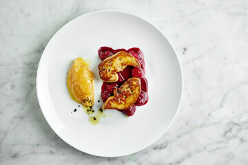 French cuisine dish - grilled foie gras liver with berry sauce and apple puree, served in a white plate on a marble background © ismishko