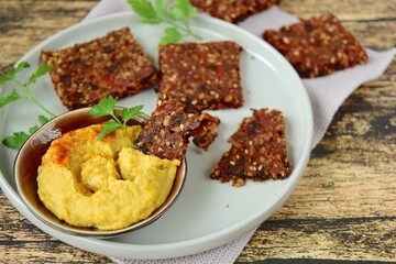 Homemade seed crackers made from bell pepper, sun dried tomato, sunflower seed, sesame seed, hemp seed and flax seeds. Served with hummus dip