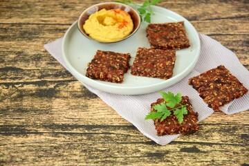 Seed crackers made from bell pepper, sun dried tomato, sunflower seed, sesame seed, hemp seed and flax seeds, garlic with parsley. Served with hummus