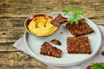 Homemade seed crackers made from bell pepper, sun dried tomato, sunflower seed, sesame seed, hemp seed and flax seeds. Served with hummus dip