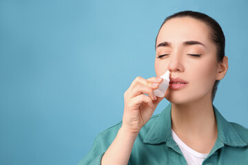 Woman using nasal spray on light blue background, space for text
