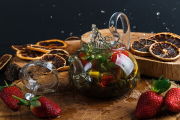 Fototapeta na wymiar Glass teapot. Still life with hot tea with lemon and strawberries. Wooden stand. Splash.