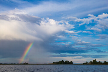 Rainbow over the river after rain on the background of blue sky in summer