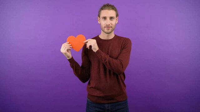 young long-haired guy with big paper red heart on isolated purple background 4k