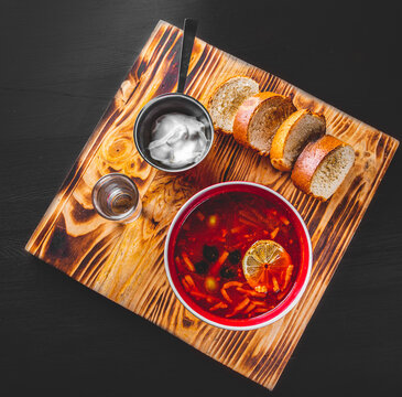 Solyanka soup with meat, sausage, vegetables, olives and lemon in bowl on black wooden table background