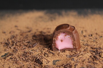 Chocolate's day enclosure chocolate candy with stuffing rests on cocoa on a grey black background with a place to text a copy of the sweet chocolate brown background