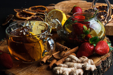 Hot tea with lemon and strawberries. Glass teapot. Wooden stand. Splash.