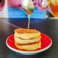 Miele mentre viene versato con un cucchiaino su dei pancake appena cotti