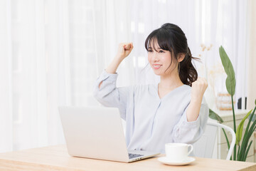 部屋でノートパソコンを使いながらガッツポーズをする若い女性