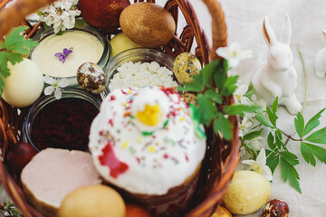 Easter food, eggs, beets, cheese, butter, ham, Easter bread in  basket with flowers on rustic table