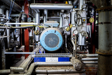 Large blue metal electric water pump turbine motor in industrial power station setting surrounded by steel pipes pressure gauges and electrical wires