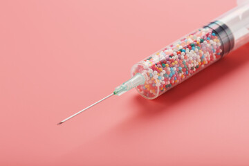 Syringe filled with colorful nano balls on a pink background.