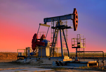 Crude oil pump jack at oilfield on atmospheric sunset backround. Fossil crude output and fuels oil...