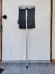 An old mop leaning against a white door