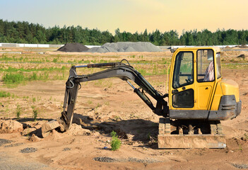 Fototapeta na wymiar Mini excavator at construction site. Backhoe on earthwork. Digg trench to lay cables concrete curbs and paving slabs. Loader on roadworks on sunset background