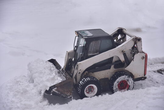 Skid-steer loader during snow removal on the road after a snowfall. Snow clearing is the job of removing snow after a snowfall to make travel easier and safer. Clearing snow concept. View from above