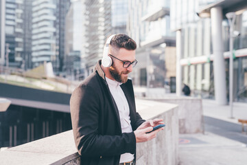 Young caucasian bearded man outdoor listening music with headphones