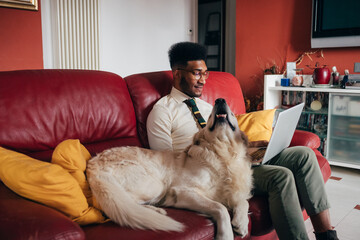 Young handsome businesslike black man lying couch using computer with his dork remote working