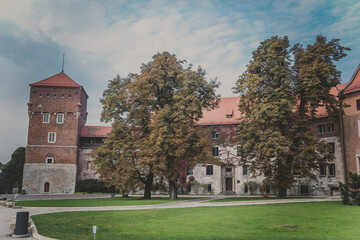 Fototapeta na wymiar View of The Thief tower and building of administration, green lawns, sidewalk and trees on Wawel Hill known as the Wawel Cathedral in Krakow Royal Castle. One of most popular landmarks in Poland