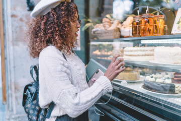 Cheerful ethnic woman choosing cake in confectionery store