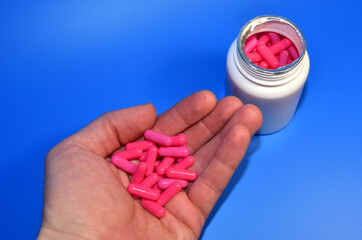 Pills in capsules in hand on blue background. Medicine grade pharmaceutical tablets. Medical pill for maintaining and improving health. Antidepressant addiction and depression concept