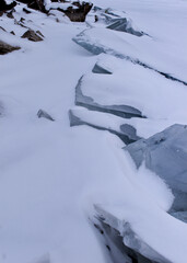 Fototapeta na wymiar Ice perched on rock from a frozen snowy lake