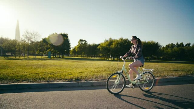 Young beautiful girl in short shorts riding a walking bicycle at sunset.